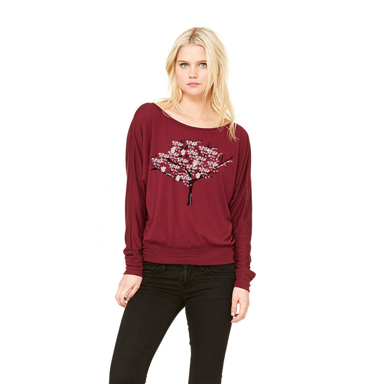 A woman wearing a burgundy long-sleeved top with a tree design on it, posing against a white background.