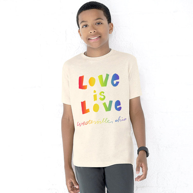 A young boy wearing a white t-shirt with the text "Love is Love" printed on it, smiling at the camera.