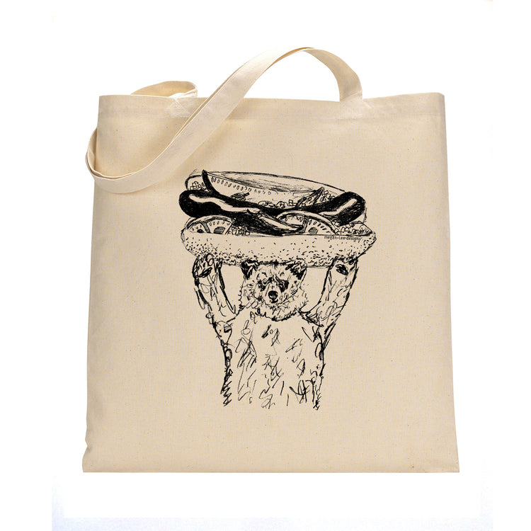 A beige tote bag with a black and white illustration of a bear holding a hot dog on its head.