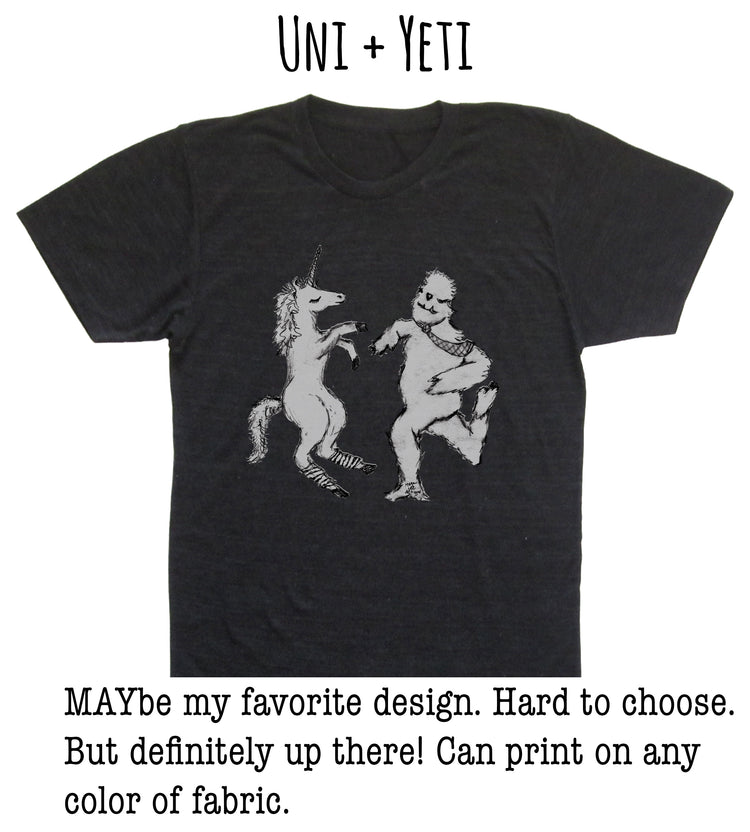 A black t-shirt with a graphic design depicting a unicorn and a creature resembling a bear or dragon. The text above the image reads "UNI + YETI".