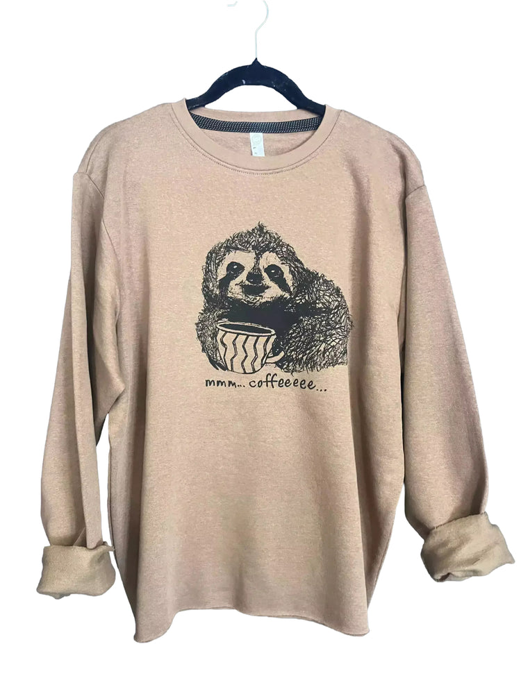 A beige long-sleeved shirt with a black and white illustration of a sloth holding a cup of coffee, accompanied by the text "mmm...coffee..."