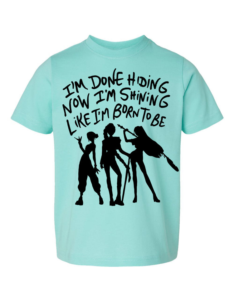A light blue t-shirt with a graphic design featuring silhouettes of three people and text that reads "I'm done hiding now I'm shining like I'm born to be".