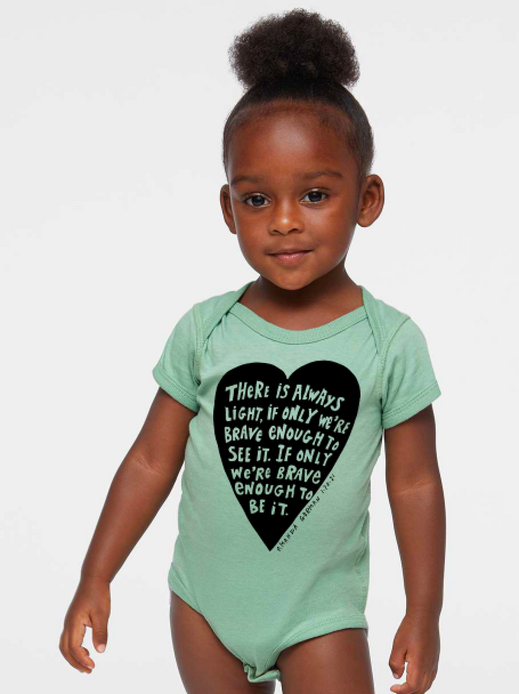 A young girl wearing a light green onesie with a heart-shaped graphic and text printed on it.