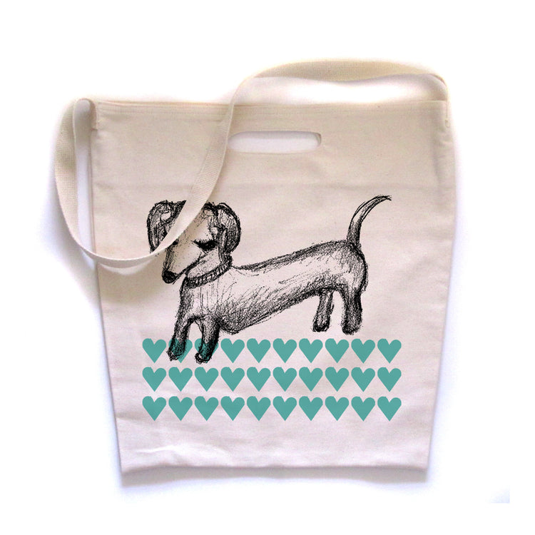 a white tote bag with a black and white illustration of a dachshund dog and a pattern of green hearts on it.