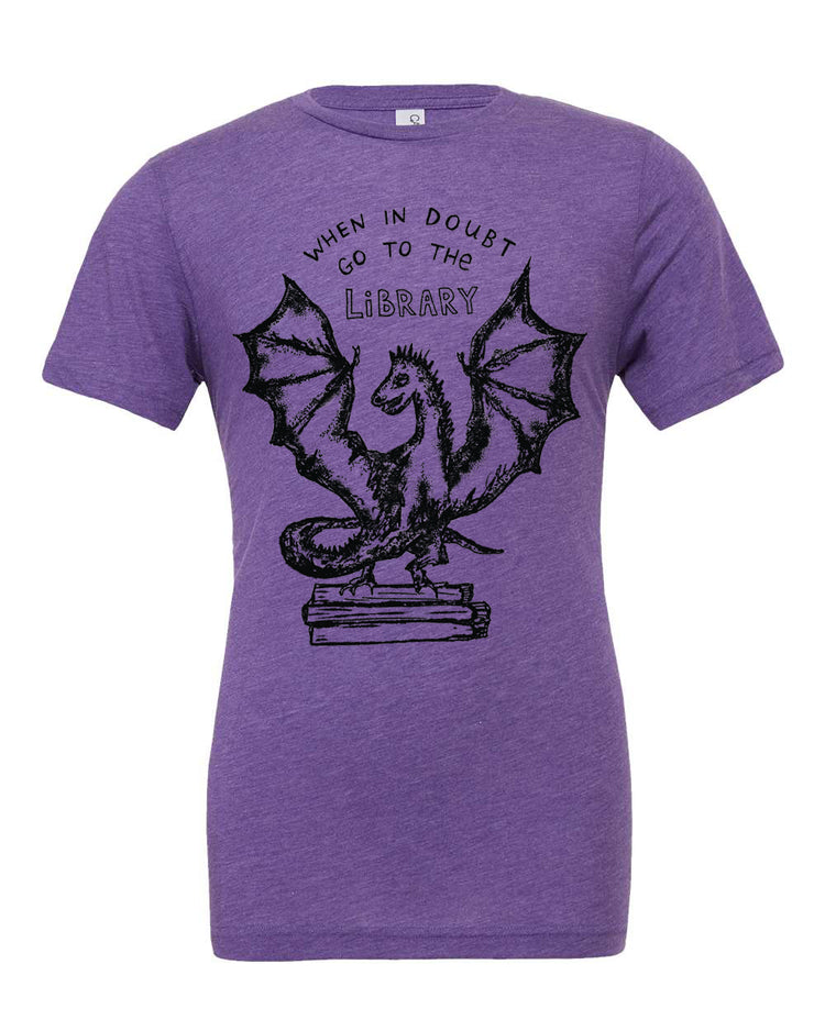 A purple t-shirt with a graphic design depicting a dragon holding a book, accompanied by the text "WHEN IN DOUBT GO TO THE LIBRARY".