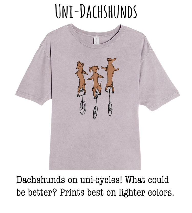 A t-shirt with a graphic design of three dachshunds riding on unicycle wheels.