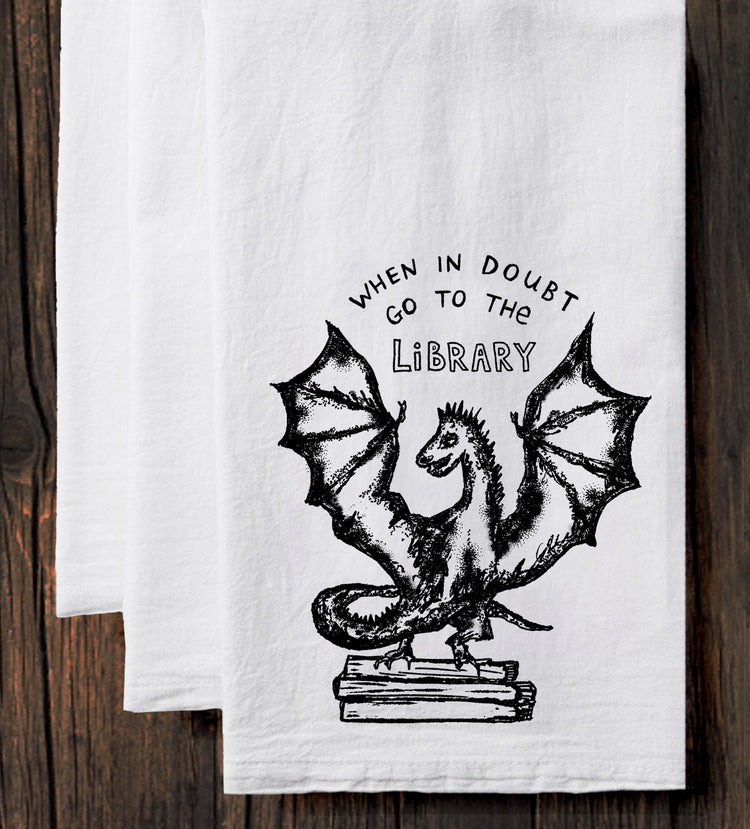 A white towel with a black illustration of a dragon and the text "WHEN IN DOUBT GO TO THE LIBRARY" printed on it.