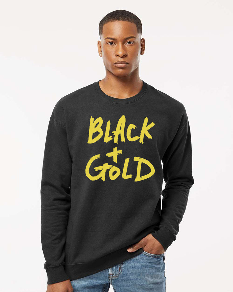 A young man wearing a black sweatshirt with the text "BLACK + GOLD" printed on it.