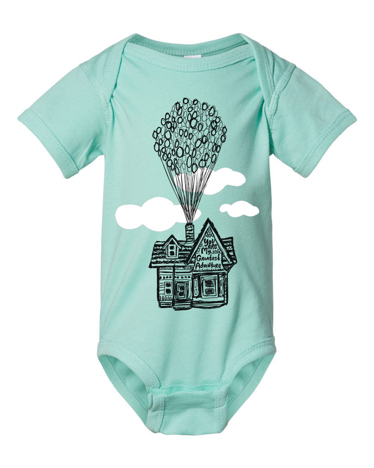 A light blue baby onesie with a graphic design depicting a house with balloons floating above it.