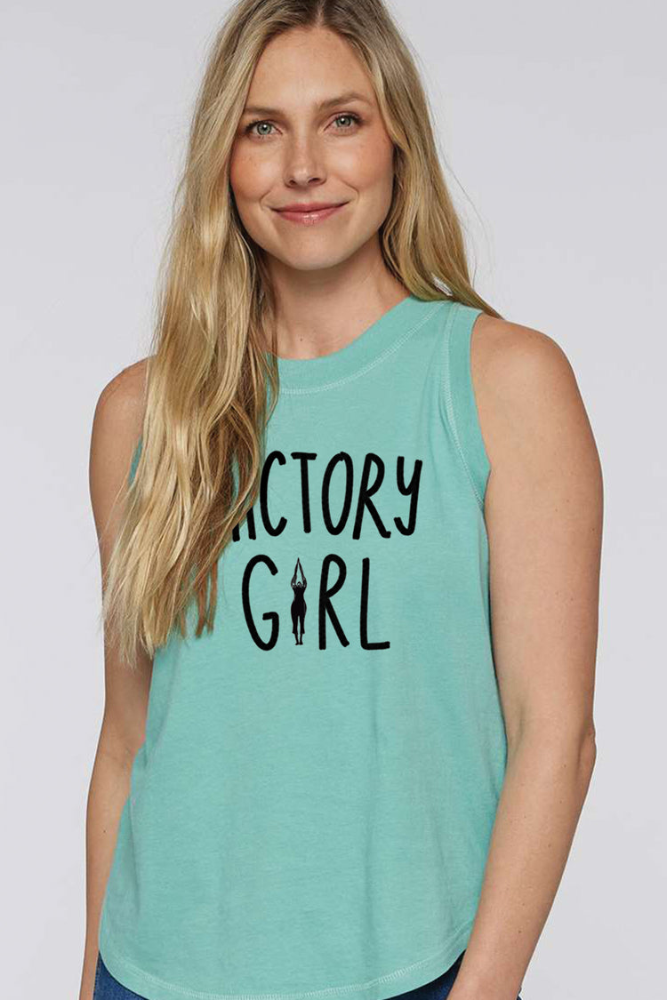 A smiling woman with long blonde hair wearing a turquoise tank top with the text "ACTORY GIRL" printed on it.