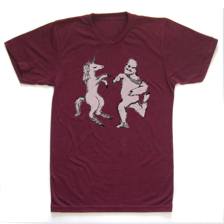 A burgundy-colored t-shirt with a graphic design depicting a unicorn and a creature resembling a Sasquatch or similar mythical being.