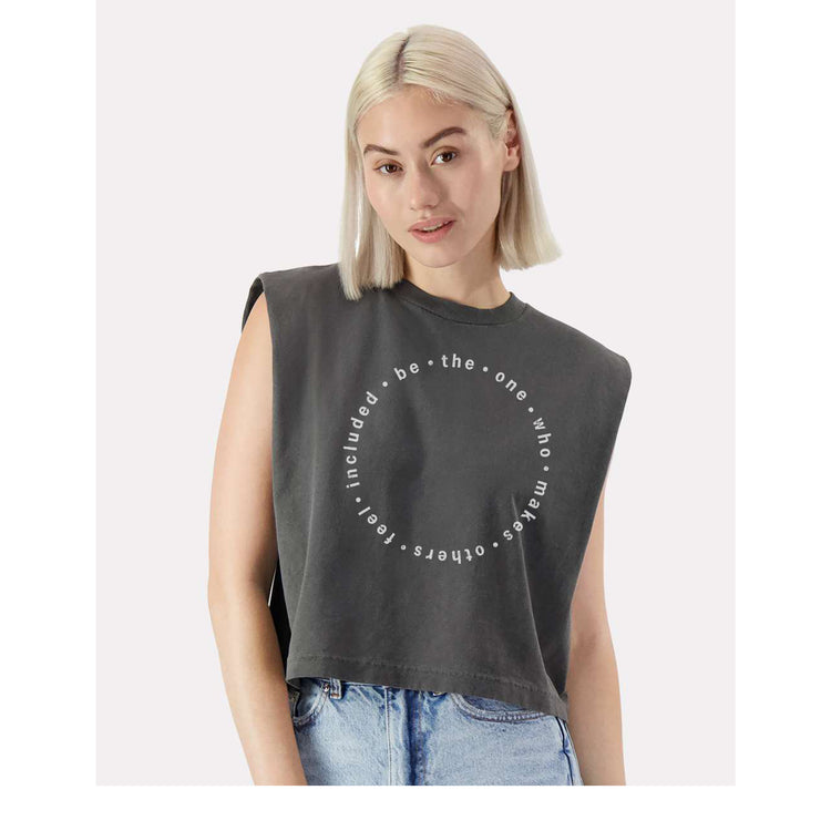 A young woman with blonde hair wearing a gray sleeveless top with a circular design on it.