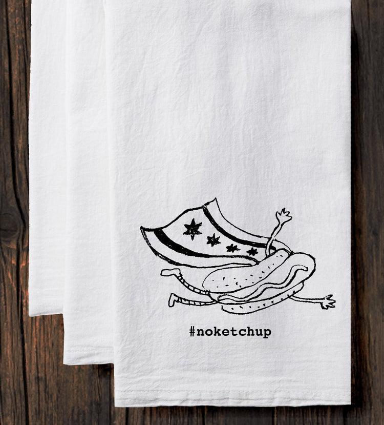 A white towel with a black and white illustration of a hot dog and a person wearing a superhero costume, along with the text "#noketchup".