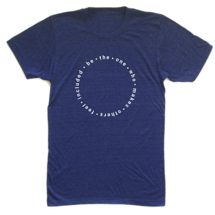 A navy blue t-shirt with a white circular design featuring the text "be the one who makes you feel included" printed on it.
