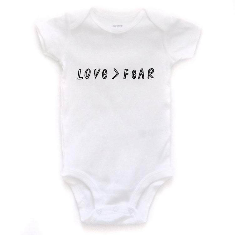 A white baby onesie with the text "LOVE > FEAR" printed on it.