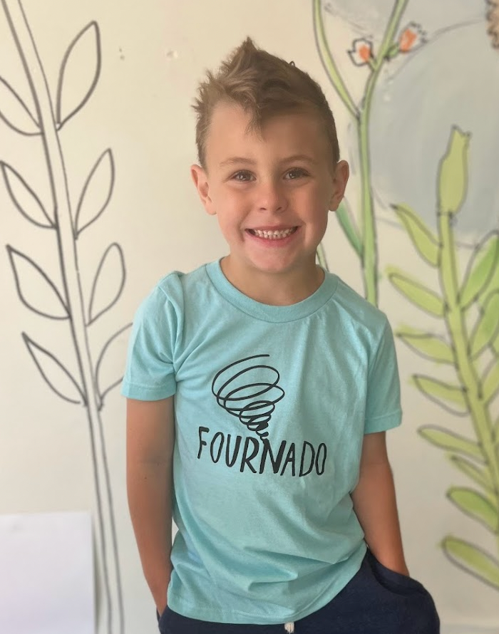 a young boy sitting in front of a flower wall