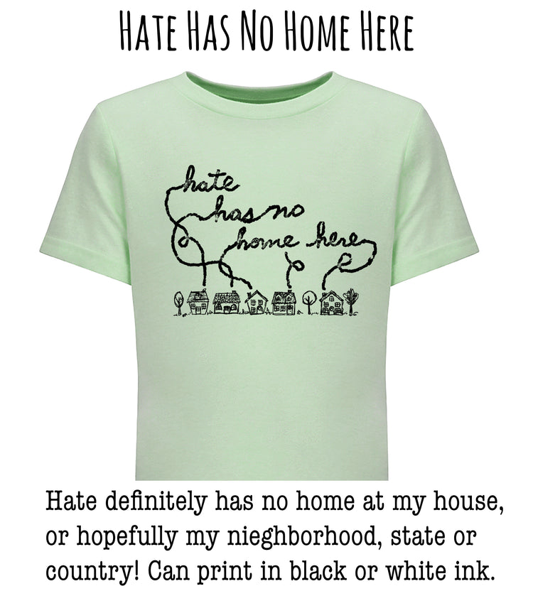 A light green t-shirt with a black handwritten message that reads " Hate has no home here" and a small illustration of houses below the text.