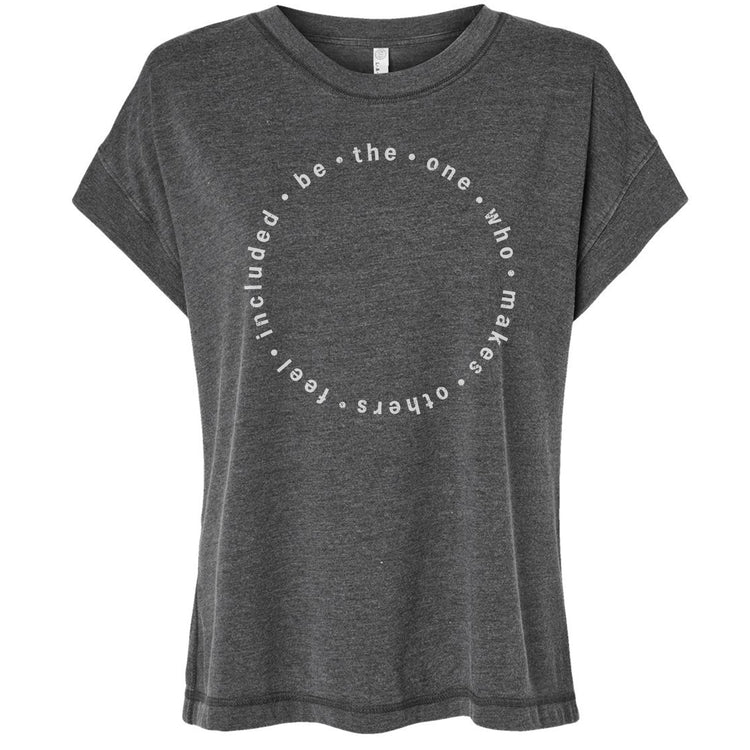 A gray t-shirt with a circular design featuring the text "be the one who makes others feel included" printed on it.