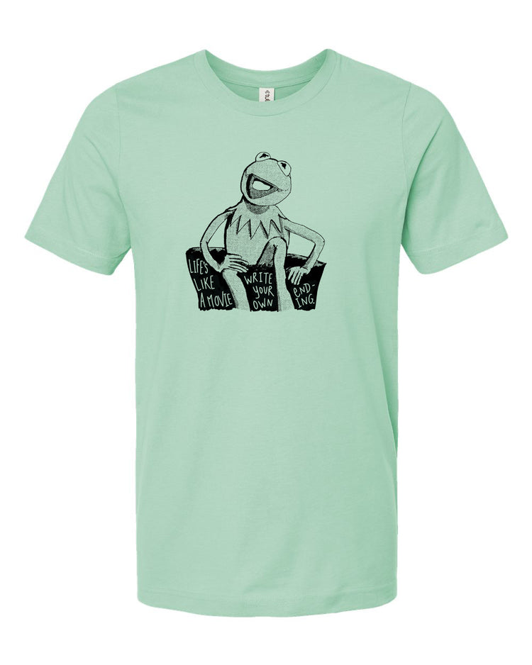 A light green t-shirt with a black and white graphic of Kermit the Frog sitting on a rock and reading a book.