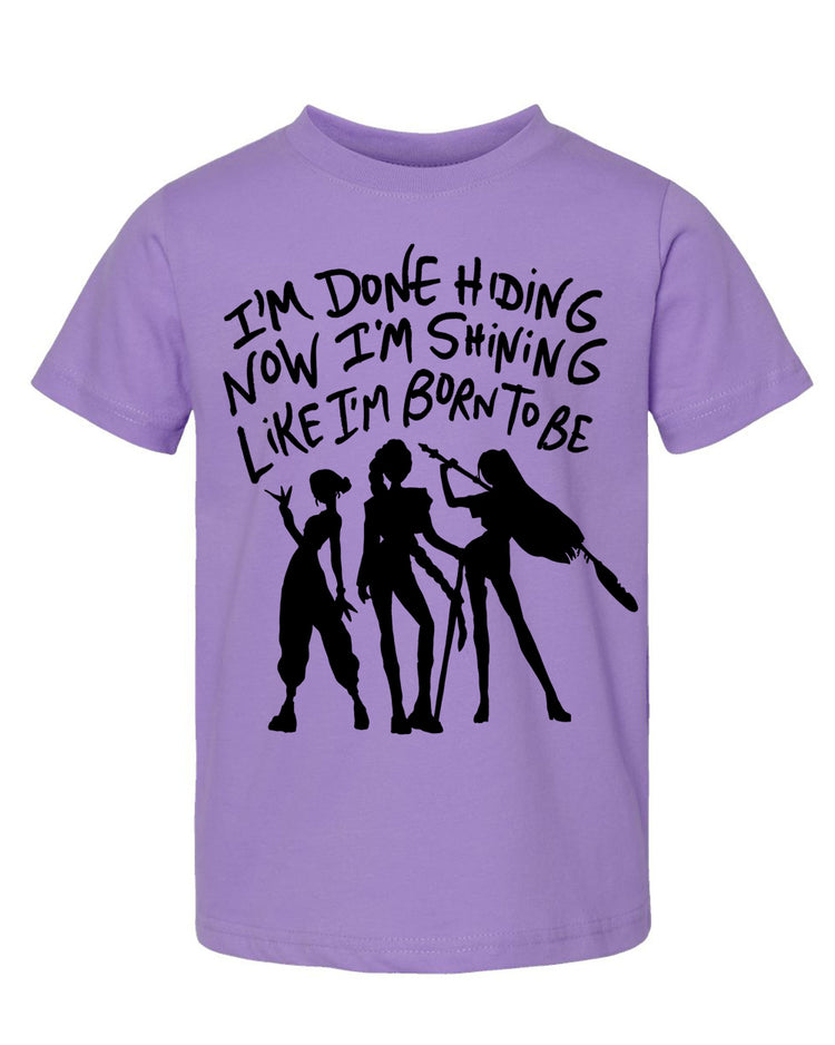 A purple t-shirt with a graphic design featuring silhouettes of three people and text that reads "I'm done hiding now I'm shining like I'm born to be".