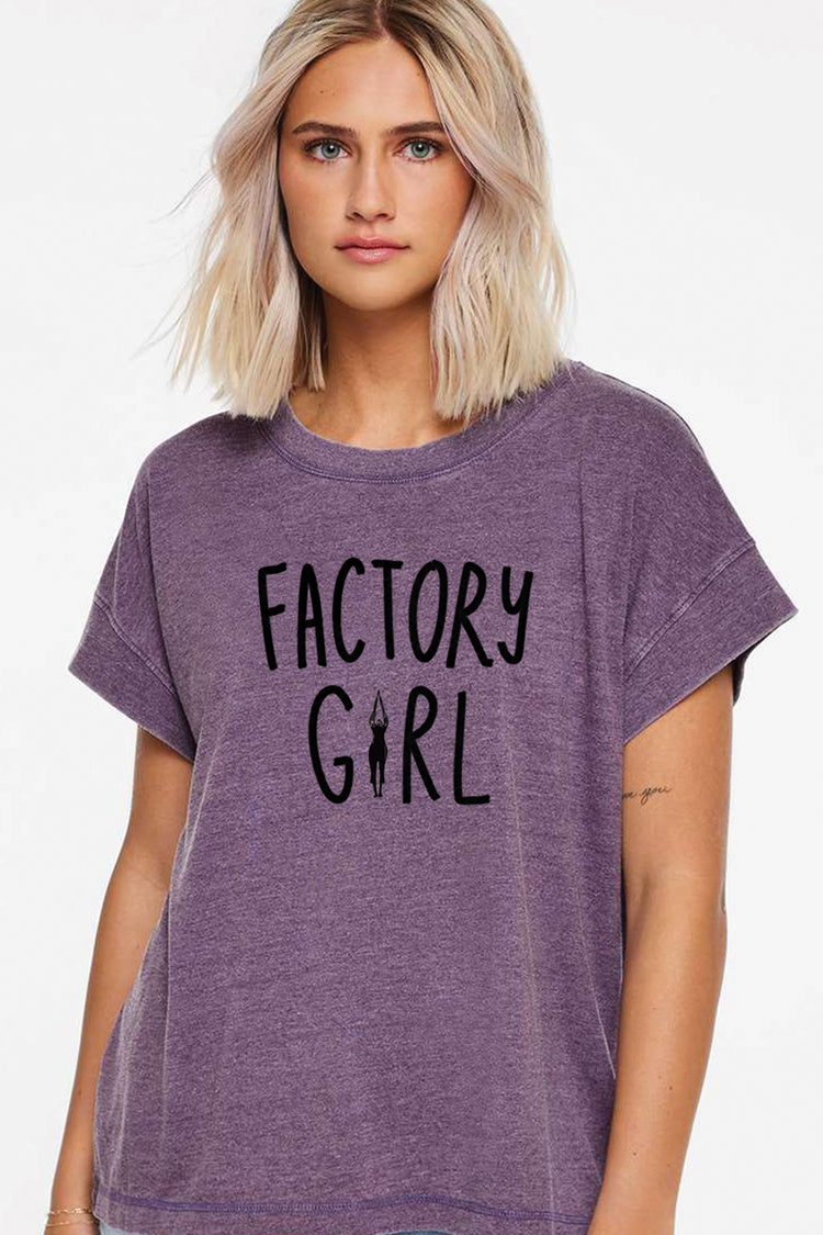 A young woman with blonde hair wearing a purple t-shirt with the text "FACTORY GIRL" printed on it.