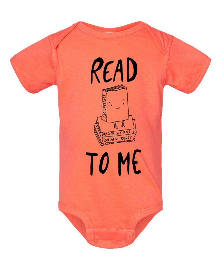 a bright orange baby onesie with a playful graphic design on it. The design includes a book with a smiling face and the text "READ TO ME" printed on it.