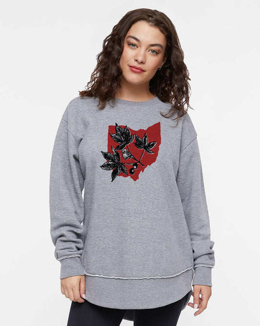 A woman wearing a grey sweatshirt with a graphic design of leaves and a red shape on it.