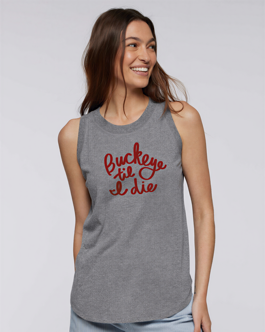 A woman wearing a gray sleeveless top with red text on it, smiling and looking to the side.