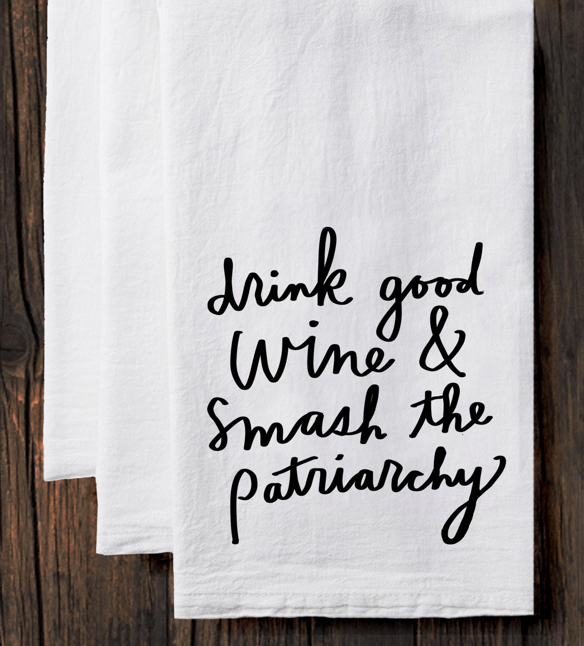 A white towel with black text printed on it, which reads "drink good wine & smash the patriarchy".