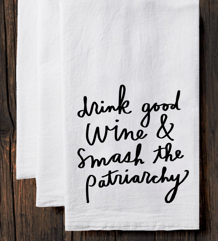 A white towel with black text printed on it, which reads "drink good wine & smash the patriarchy".