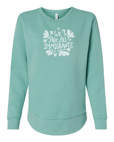 A mint green sweatshirt with a white graphic design on the front that reads "We Are All Immigrants".