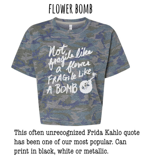a gray camouflage t-shirt with a white text quote that reads "Not like a flower, fragile like a bomb" and a small white explosion symbol. The quote is often unacknowledged and has been one of our most popular. The t-shirt can be printed in black, white, or metallic colors.
