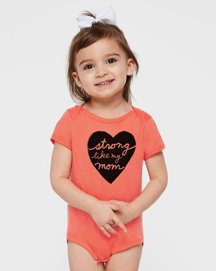 A young girl wearing a bright orange onesie with a heart design and the text "Strong like my mom" printed on it.