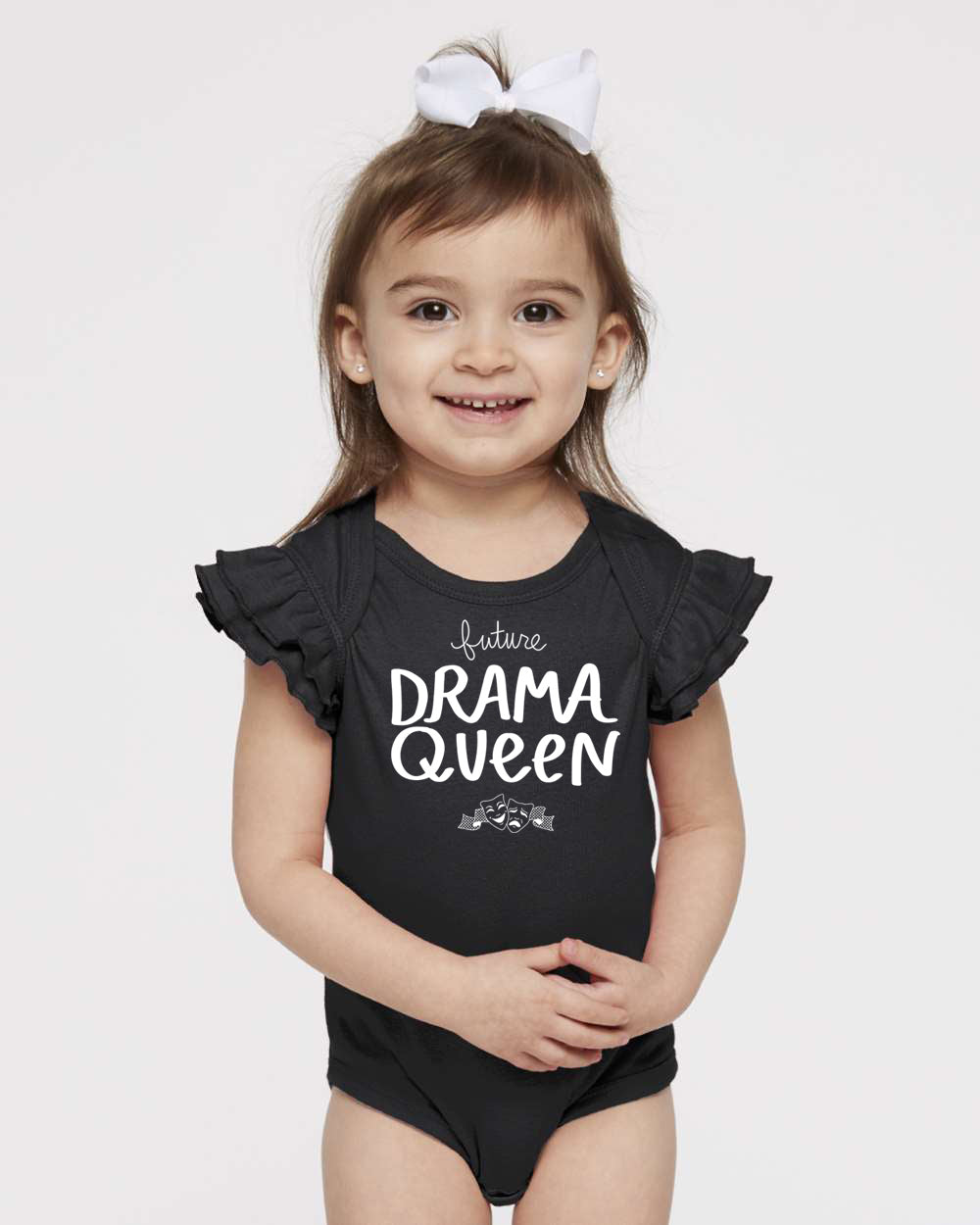 A young girl wearing a black ruffled swimsuit top with the text "Future Drama Queen" printed on it, smiling at the camera.
