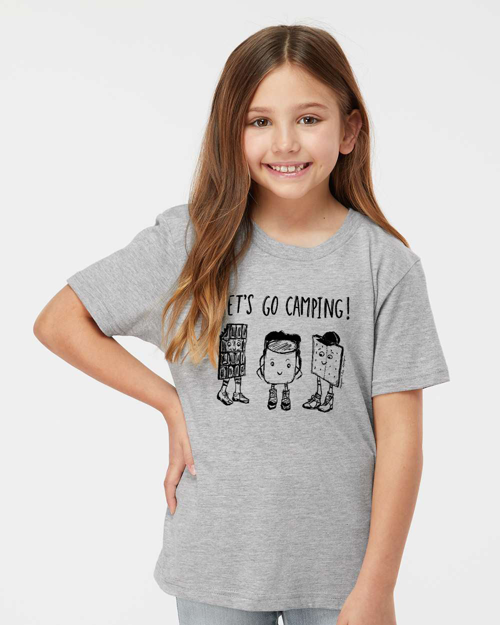 A young girl with long brown hair is smiling and wearing a gray t-shirt with a graphic design featuring three cartoon characters and the text "Let's go camping!"