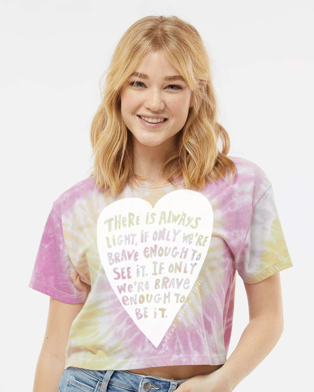 A smiling young woman wearing a tie-dye shirt with a heart-shaped design and text printed on it.