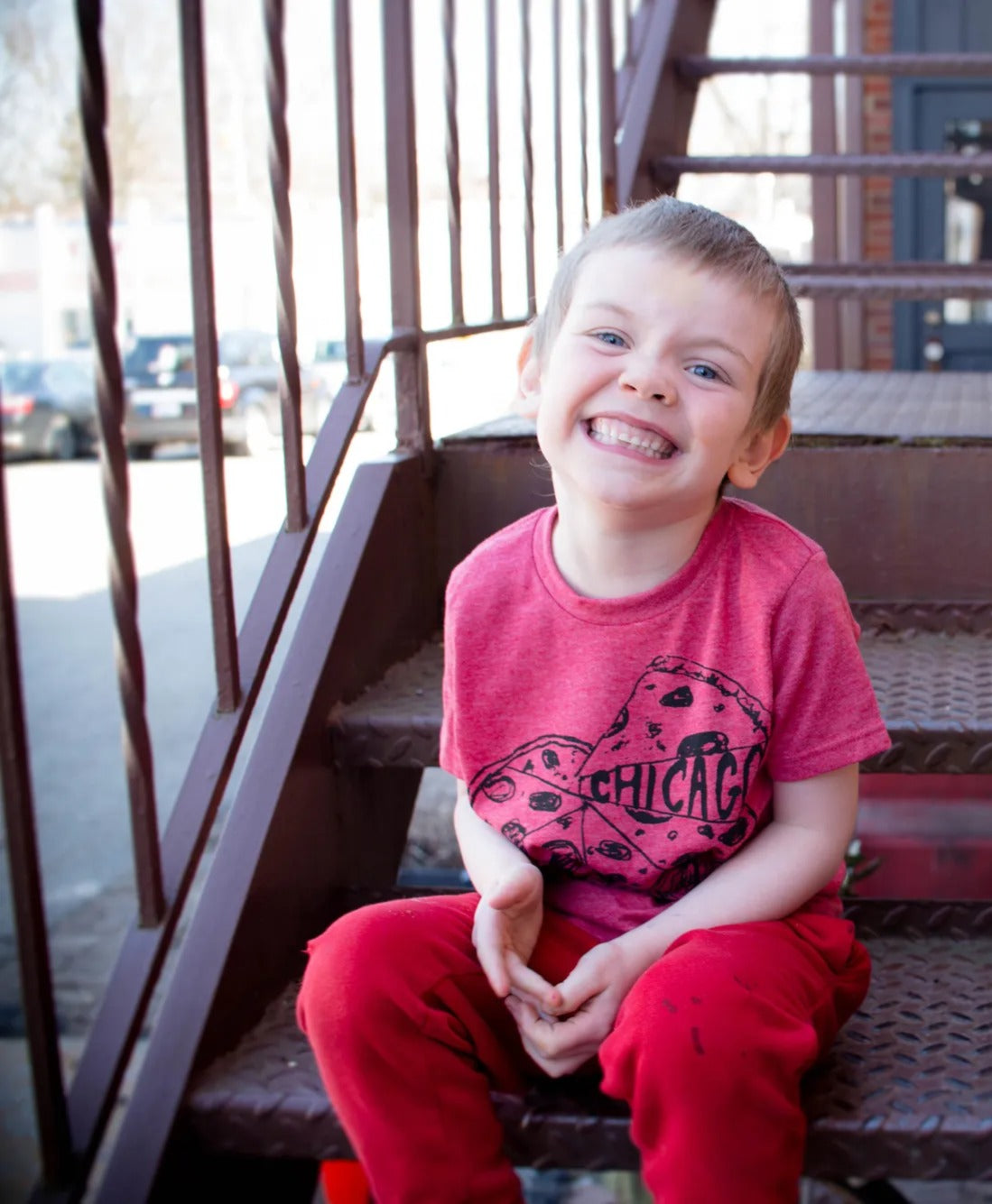 Two young boys sitting on a staircase, smiling and wearing colorful t-shirts.