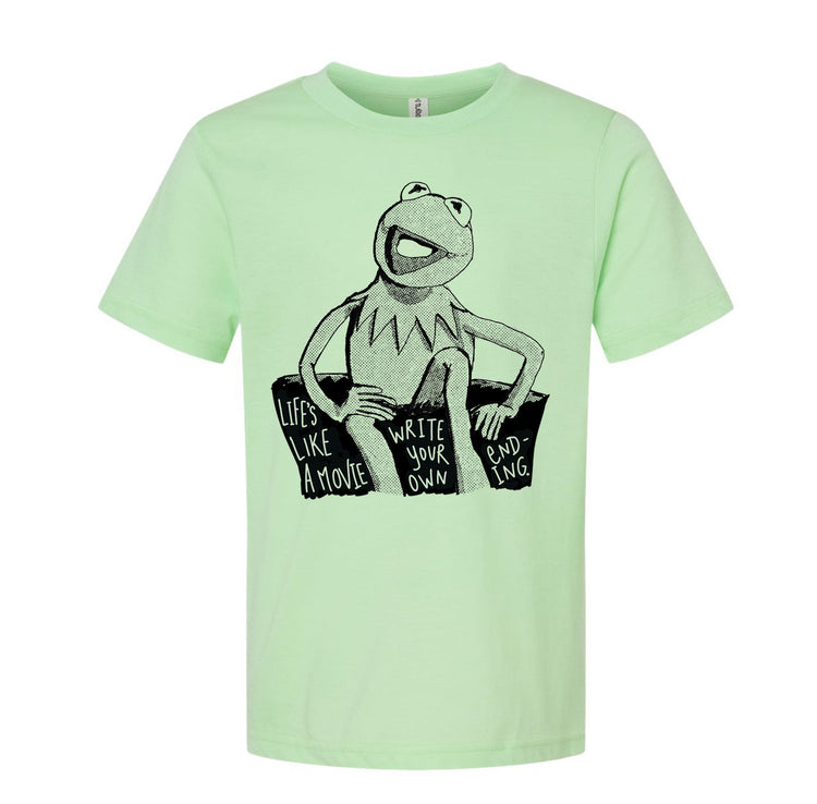 A light green t-shirt with a black and white illustration of Kermit the Frog sitting on a rock and the text "Lives like a movie, write your own ending" printed on it.