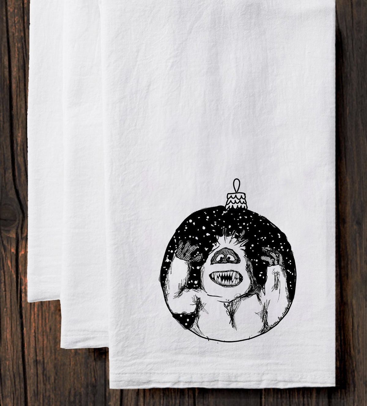 A white towel with a black and white illustration of a monster or monster-like creature on it, along with a Christmas ornament.