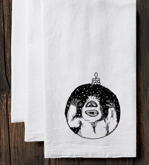 A white towel with a black and white illustration of a monster or monster-like creature on it, along with a Christmas ornament.