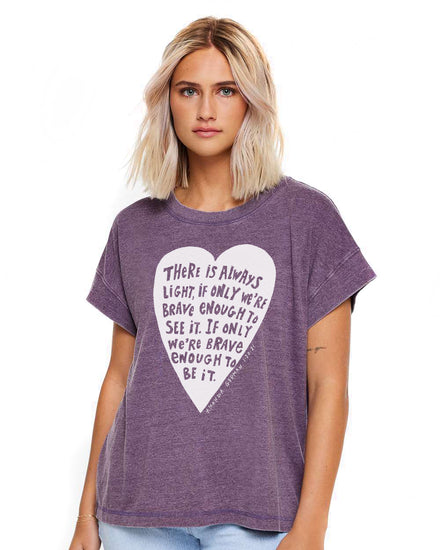 A young woman with blonde hair wearing a purple t-shirt with a heart-shaped graphic and text printed on it.