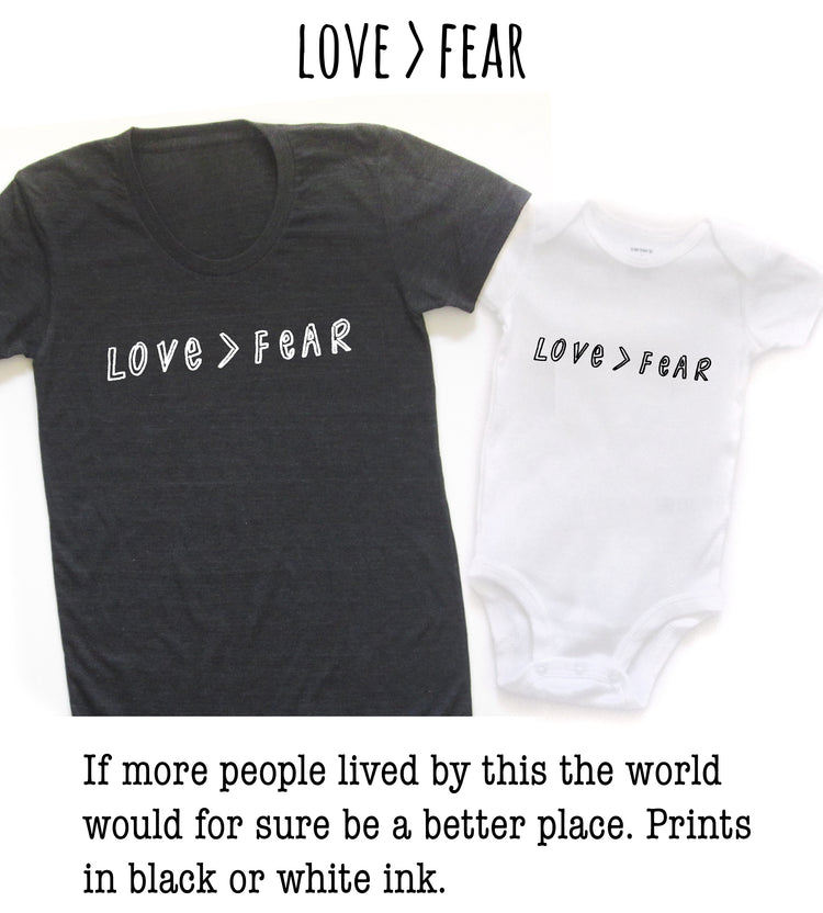 two t-shirts, one black and one white, with the text "LOVE > FEAR" printed on them.