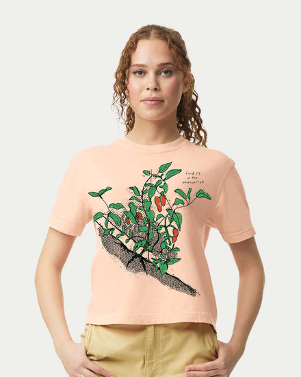 A woman wearing a peach-colored t-shirt with a graphic of a plant and text on it.