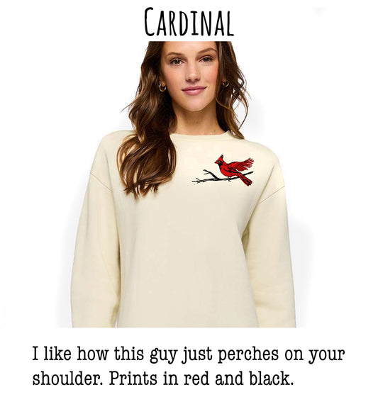 A woman wearing a cream-colored sweater with a red cardinal bird embroidered on the front, posing for a photograph.