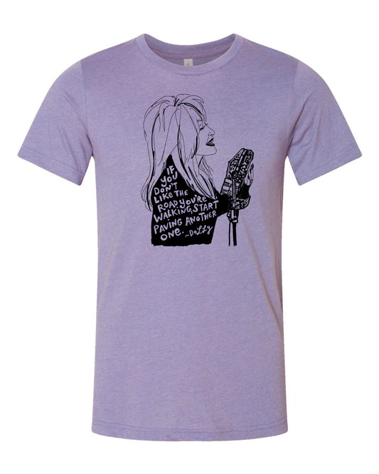 A graphic t-shirt design featuring a stylized illustration of a woman with long hair and a serious expression, accompanied by text that reads "If you don't like the road you're on, start walking another one. Dolly".