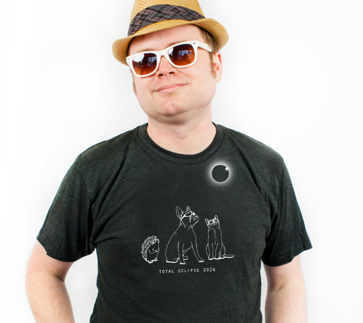 A man wearing a hat and sunglasses is posing for a photo, with a graphic t-shirt featuring a graphic of a solar eclipse and the text "Total Eclipse 2034".