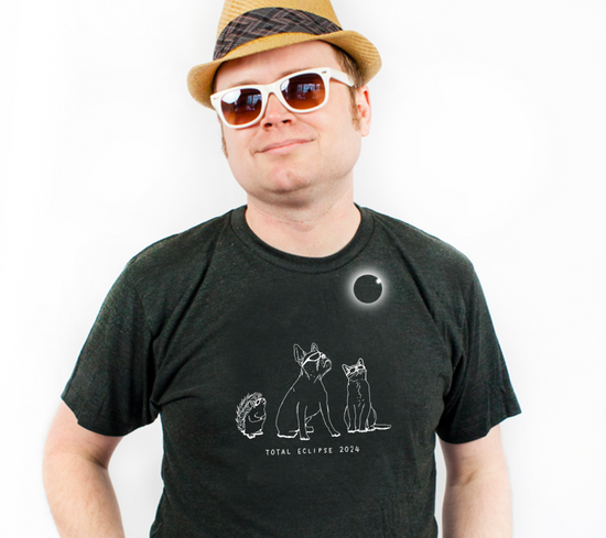 A man wearing a hat and sunglasses is posing for a photo, with a graphic t-shirt featuring a graphic of a solar eclipse and the text "Total Eclipse 2034".
