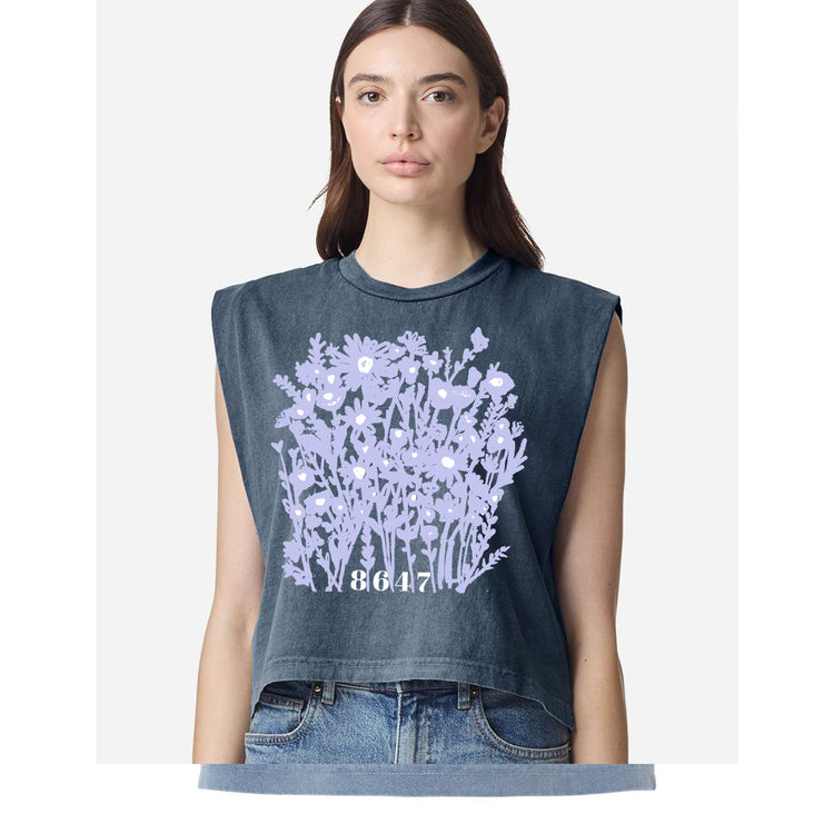 A woman wearing a gray sleeveless top with a graphic design of purple flowers and the number "8647" printed on it.