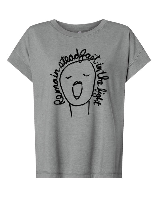 A gray t-shirt with a simple black and white graphic design depicting a face with an open mouth and the text " Remain steady fast in the light" written around the face.