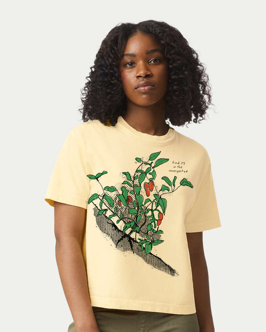 A young woman with curly hair wearing a yellow t-shirt with a graphic of a plant or tree on it.